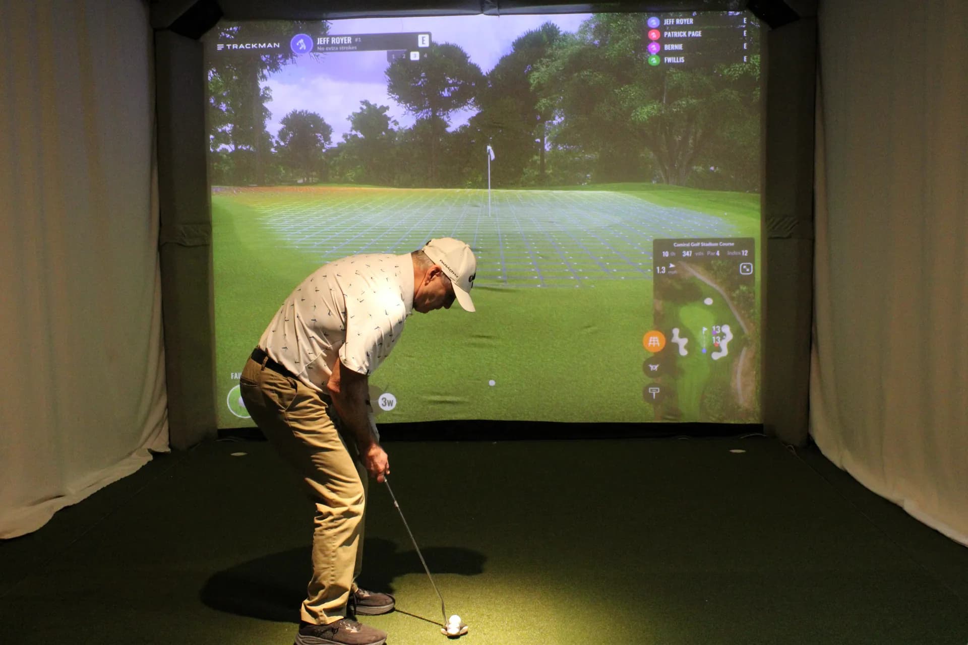 Player in white polo and khakis mid-swing in a TrackMan simulator at Gonzo's HD Sports