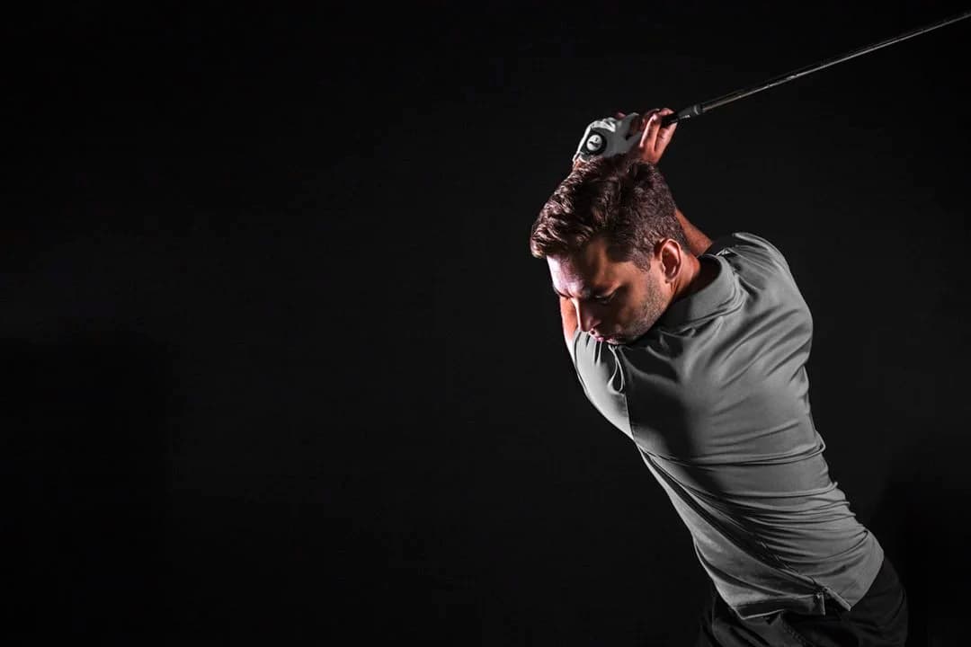 Golfer mid-swing in a dark, atmospheric TrackMan simulator bay at night