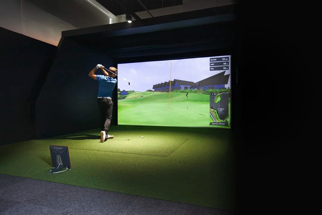 Golfer swinging in a TrackMan simulator bay with course data on screen